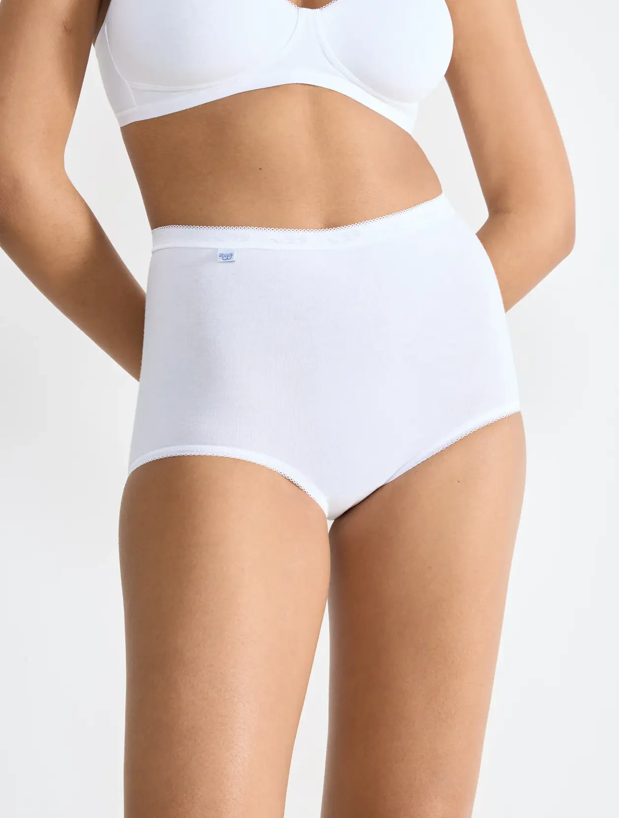 Kalhotky Sloggi Basic+ 10007656 – bílé klasické dámské bavlněné kalhotky s vysokým pasem, modelka od pasu po stehna na bílém pozadí