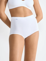 Kalhotky Sloggi Basic+ 10007656 – bílé klasické dámské bavlněné kalhotky s vysokým pasem, modelka od pasu po stehna na bílém pozadí
